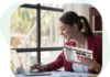 Woman in red jacket reading flyer and working on laptop.